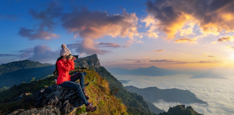 Nepal travel deals traveller sitting rock holding camera take photo doi pha mon mountains chiang rai thailand