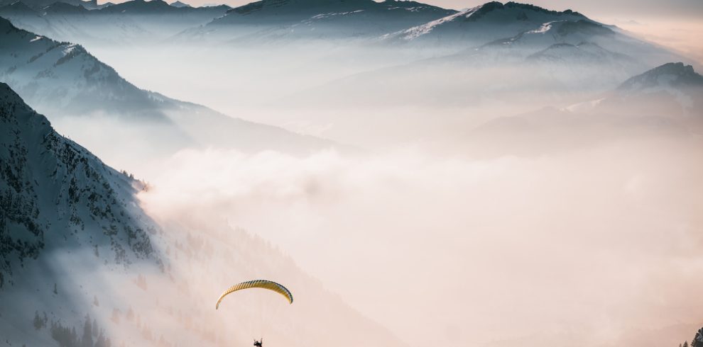 Nepal travel deals aerial shot person parachuting down clouds near snowy mountains